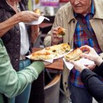 Vier Personen teilen sich im Freien Gebäck und halten Servietten.