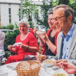 Eine Gruppe von Menschen lächelt und genießt gemeinsam eine Mahlzeit an einem Tisch im Freien.