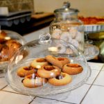 Verschiedene Kekse und Gebäck unter Glaskuppeln auf einer gefliesten Arbeitsplatte in einer Bäckerei.