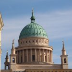 Kathedrale mit grüner Kuppel, Säulen und Türmen unter blauem Himmel, teilweise eingerahmt von angrenzenden Gebäuden.