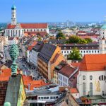 Luftaufnahme von Augsburg, Deutschland, mit farbenfrohen Gebäuden, Kirchtürmen und einer belebten Straße.