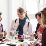 Eine Gruppe von Menschen genießt gemeinsam eine Mahlzeit an einem Tisch in der Nähe eines Fensters.