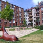 Eine Pferdestatue in einem grasbewachsenen Innenhof, umgeben von Backsteinwohnhäusern und Bäumen.