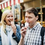 Ein Mann und eine Frau genießen ein Eis vor einem Café mit einer rot-weiß gestreiften Markise.