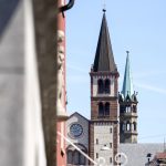 Blick auf eine Kirche mit Glockenturm und Turmspitze vor einem klaren blauen Himmel.