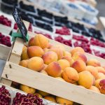 Frische Pfirsiche und Beeren, die auf einem Markt in Holzschalen ausgestellt sind.