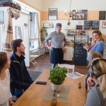 Leute, die an einem Tisch sitzen und einer Person zuhören, die in einem Café steht.