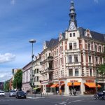 Eine belebte städtische Kreuzung mit einem historischen Gebäude mit einem Uhrenturm und einem Café mit Sitzgelegenheiten im Freien.