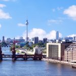 Stadtbild von Berlin mit Spree, Oberbaumbrücke und Fernsehturm unter blauem Himmel mit vereinzelten Wolken.