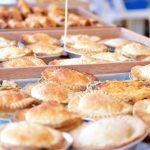 Eine Auswahl frisch gebackener Kuchen in Holztabletts, die an eine gemütliche Lübecker Bäckerei erinnern, warten auf Ihren Genuss auf dem Tisch. Perfekt für jeden Anlass, vielleicht auch als süße Leckerei während eines Betriebsausflugs.