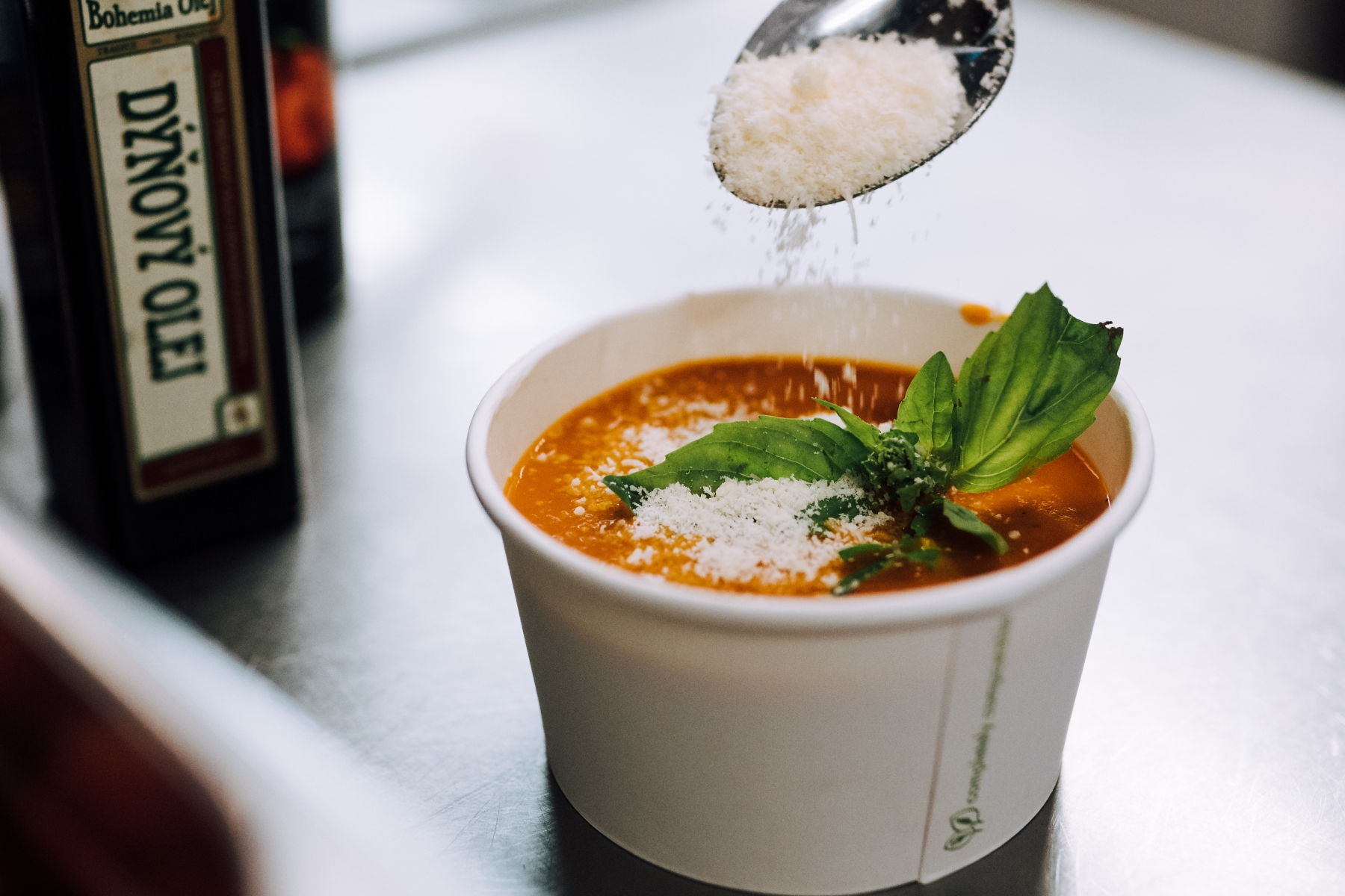 Eine köstliche Schüssel Suppe, garniert mit geriebenem Käse und Basilikumblättern, steht einladend neben einer Flasche Öl, perfekt zum Genießen nach einem lustigen Betriebsausflug.