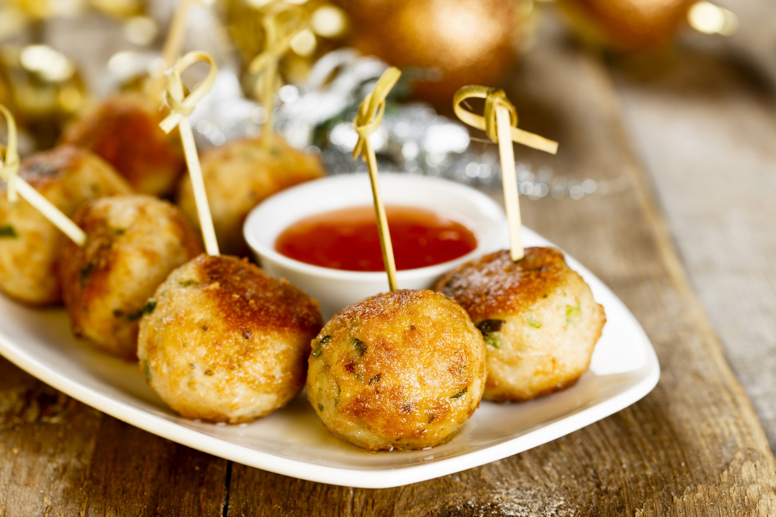 Hähnchenfleischbällchen am Spieß mit pikanter Dip-Sauce, elegant angerichtet auf einem weißen Teller, perfekt, um jedes Betriebsausflug-Treffen auf einem rustikalen Holztisch zu verschönern.