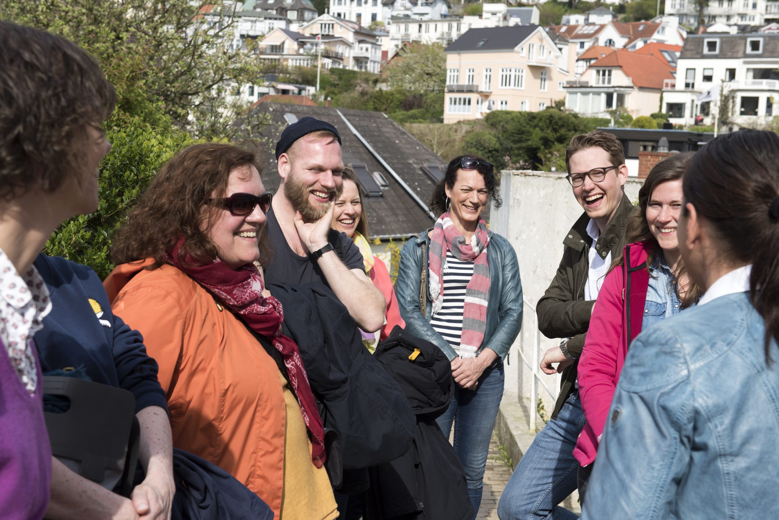 Eine Gruppe von Menschen genießt einen Betriebsausflug, lächelt und plaudert im Freien in einem Wohngebiet mit charmanten Häusern im Hintergrund.