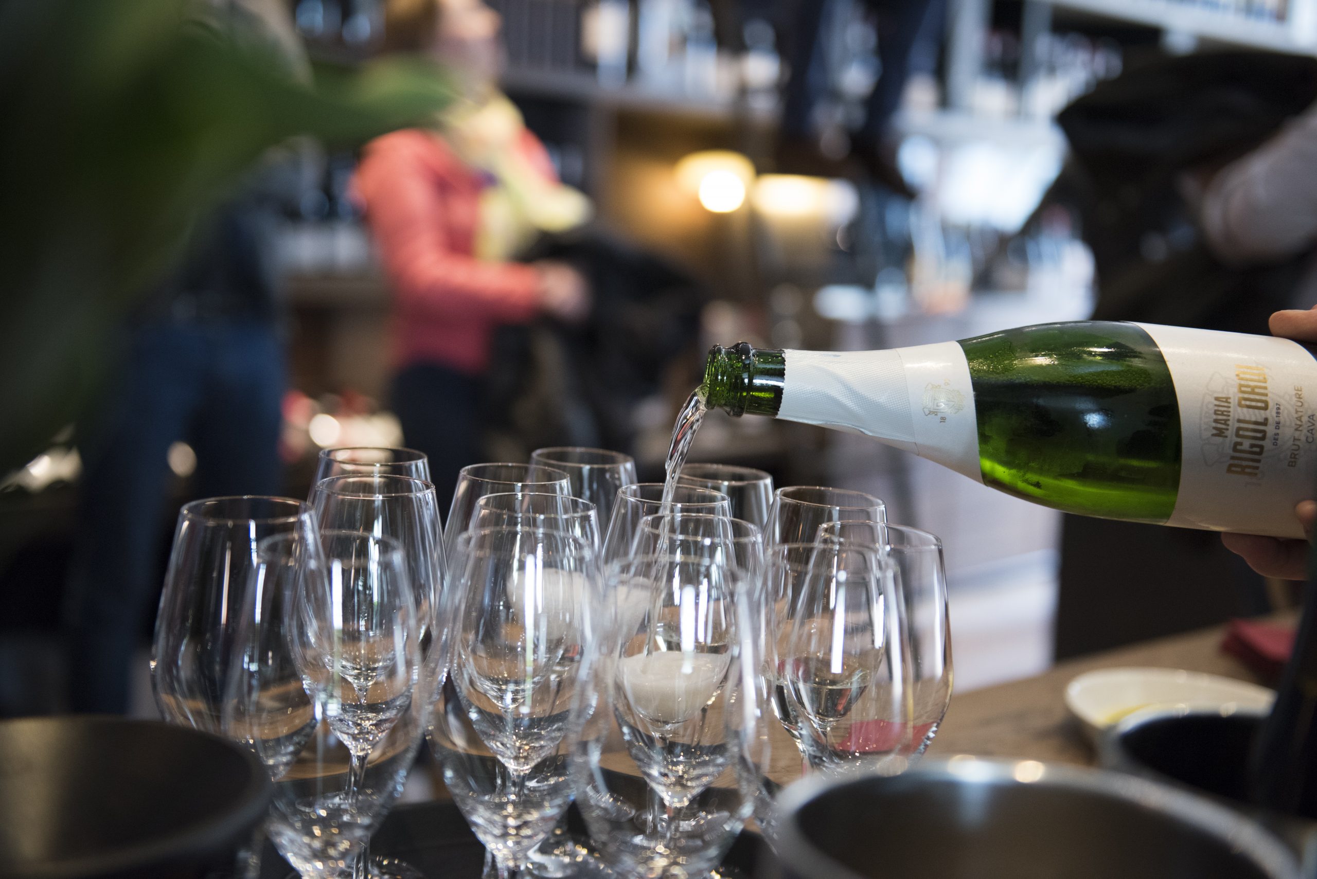 Bei einem lebhaften Betriebsausflug wird Champagner in mehrere klare Gläser auf dem Tisch gegossen, um die fröhliche Stimmung des Anlasses einzufangen.