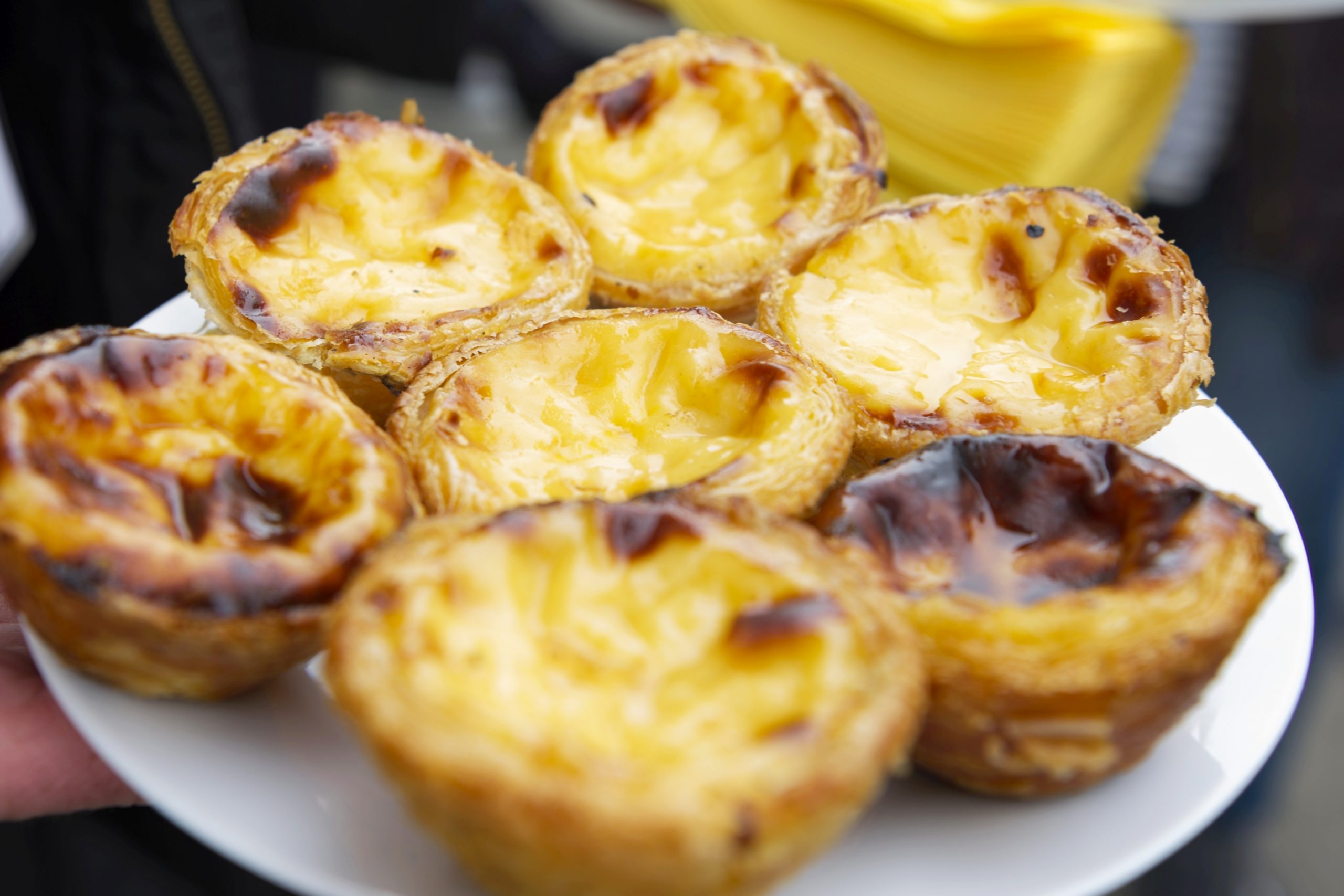 Ein Teller mit glänzenden portugiesischen Puddingtörtchen, perfekt als süße Leckerei während eines Betriebsausflugs, mit knuspriger, karamellisierter Oberfläche aus der Nähe.