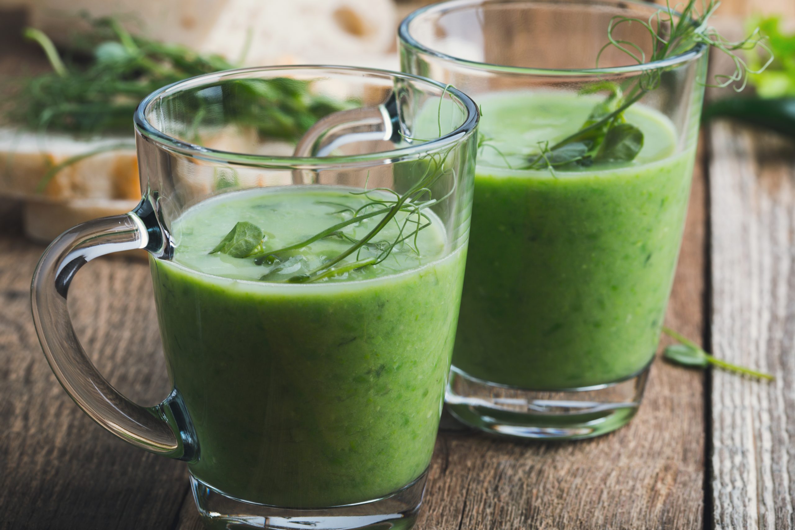 Auf dem Holztisch stehen zwei durchsichtige Becher, gefüllt mit grünem Smoothie, garniert mit Erbsensprossen – eine bildschöne Erfrischung für jeden Betriebsausflug.