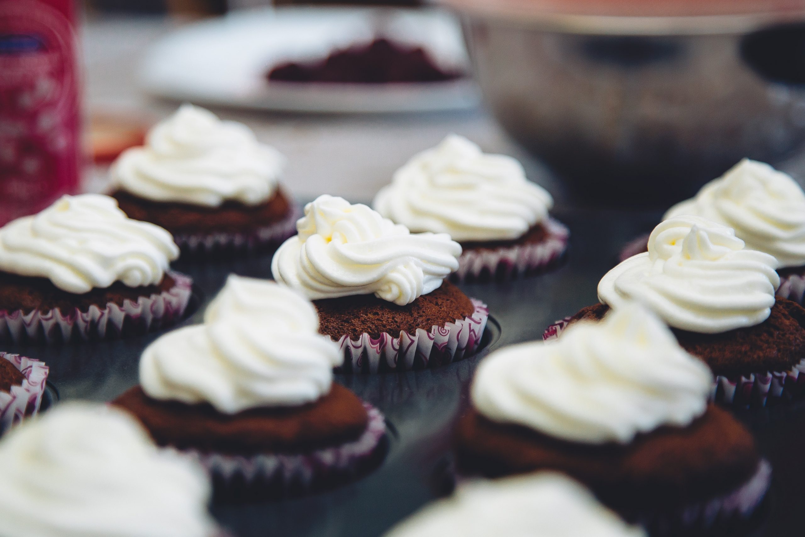 Mit Wirbeln aus weißem Zuckerguss verzierte Schokoladen-Cupcakes, angeordnet auf einer reflektierenden Oberfläche, sind der perfekte süße Leckerbissen während eines Betriebsausflugs.