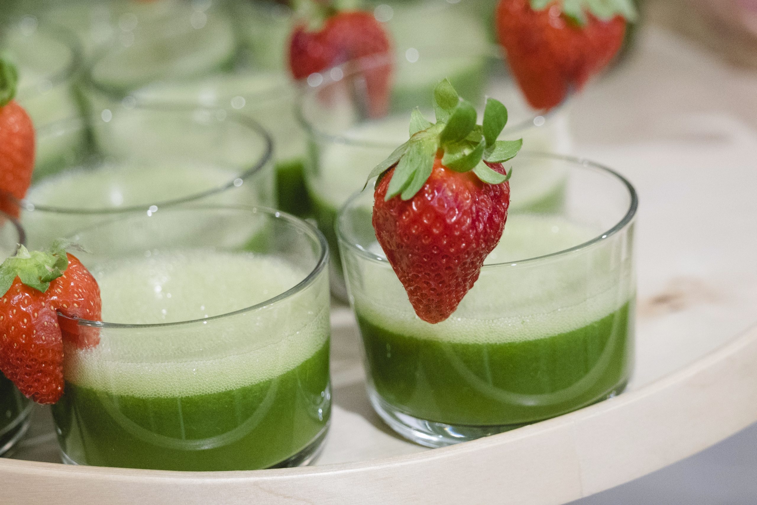 Gläser grüner Saft mit Schaum, perfekt für Ihren nächsten Betriebsausflug, jedes mit einer frischen Erdbeere garniert.