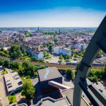 Luftaufnahme einer Stadtlandschaft mit städtischen Gebäuden, Grünflächen und Bahngleisen unter einem klaren blauen Himmel.