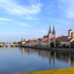 Malerische Aussicht auf eine europäische Stadt mit einem Fluss, historischen Gebäuden und einer Kathedrale unter einem blauen Himmel.