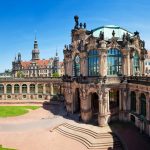 Kunstvolle Barockarchitektur des Dresdner Zwingers mit blauem Himmel und viel Grün.