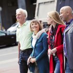 Vier Menschen gehen gemeinsam eine Stadtstraße entlang, lächeln und genießen ihre Umgebung.