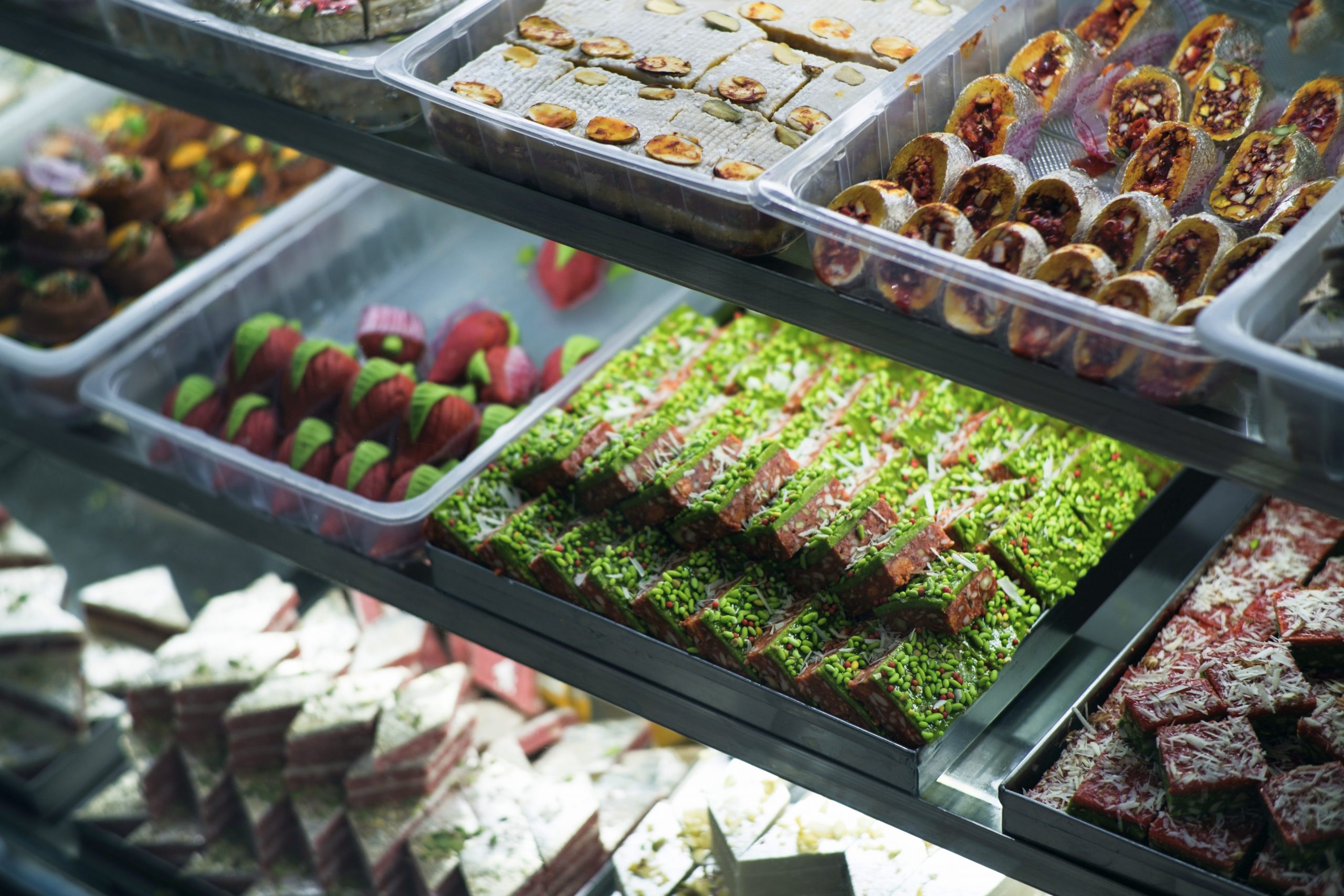 Es erwartet Sie ein herrliches Erlebnisgastronomie-Erlebnis mit einer Auswahl an farbenfrohem Gebäck und Süßigkeiten, die in einer Glasvitrine im Konditoreiladen elegant präsentiert werden.