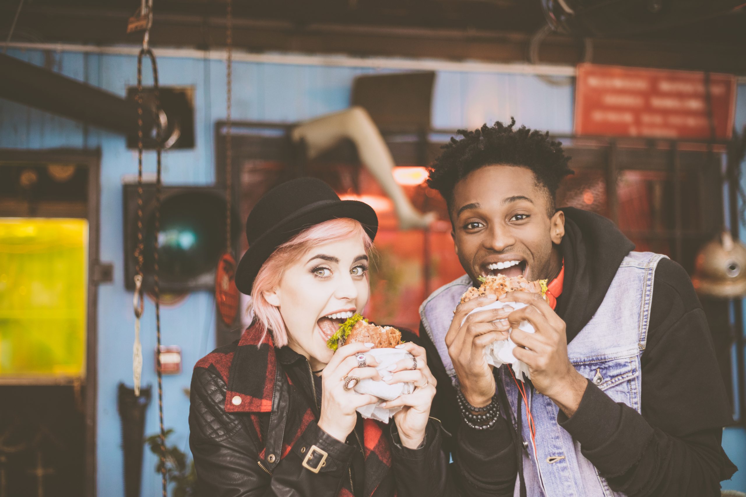 Zwei Menschen genießen glücklich Burger im Innenbereich, umgeben von einer lebendigen Kulisse, die ihre Mahlzeit zu einem Erlebnisgastronomie-Erlebnis macht.