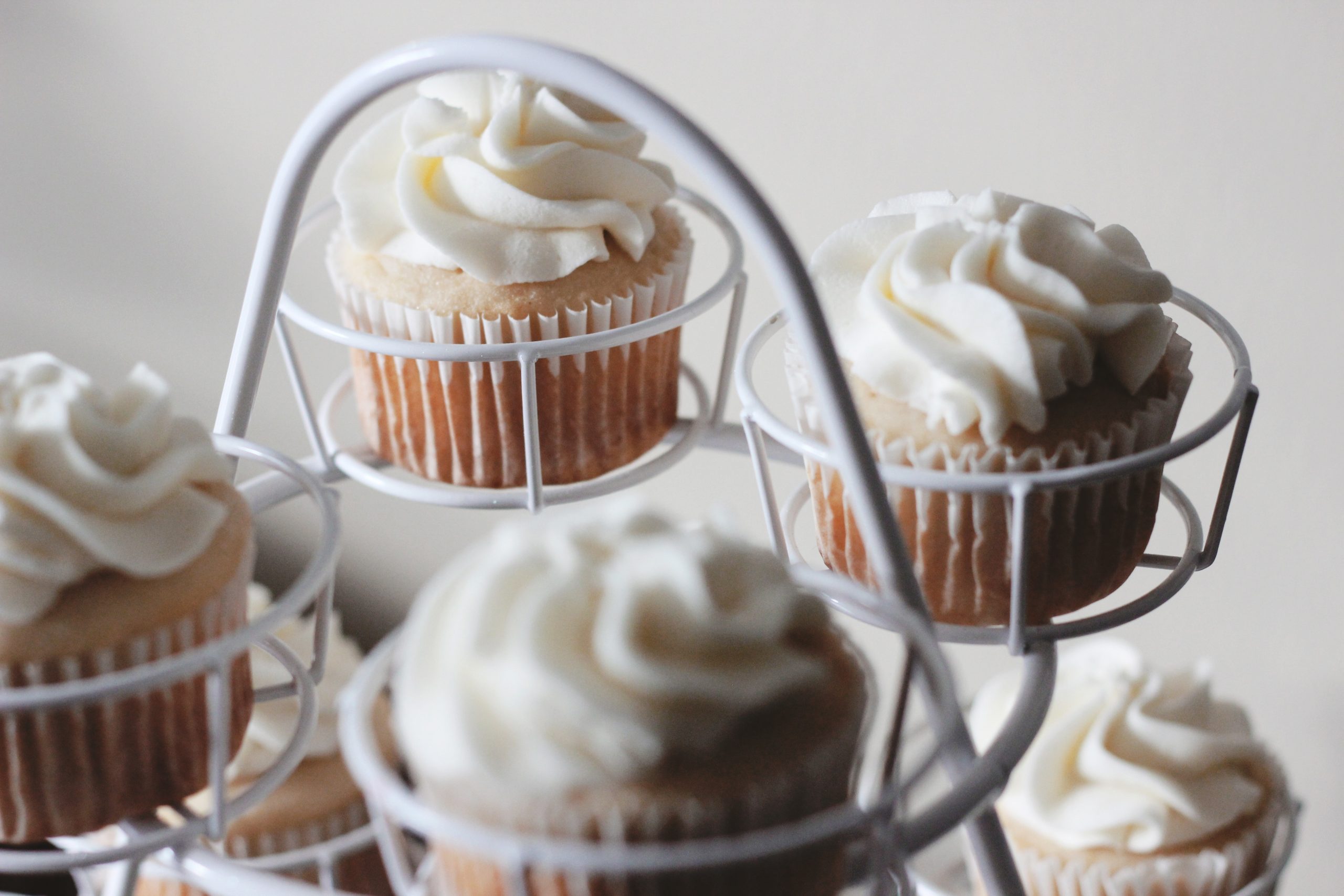 Cupcakes mit weißem Zuckerguss werden kunstvoll auf einem Metallständer präsentiert und verleihen Ihrem kulinarischen Erlebnis einen herrlichen Hauch von Erlebnisgastronomie.