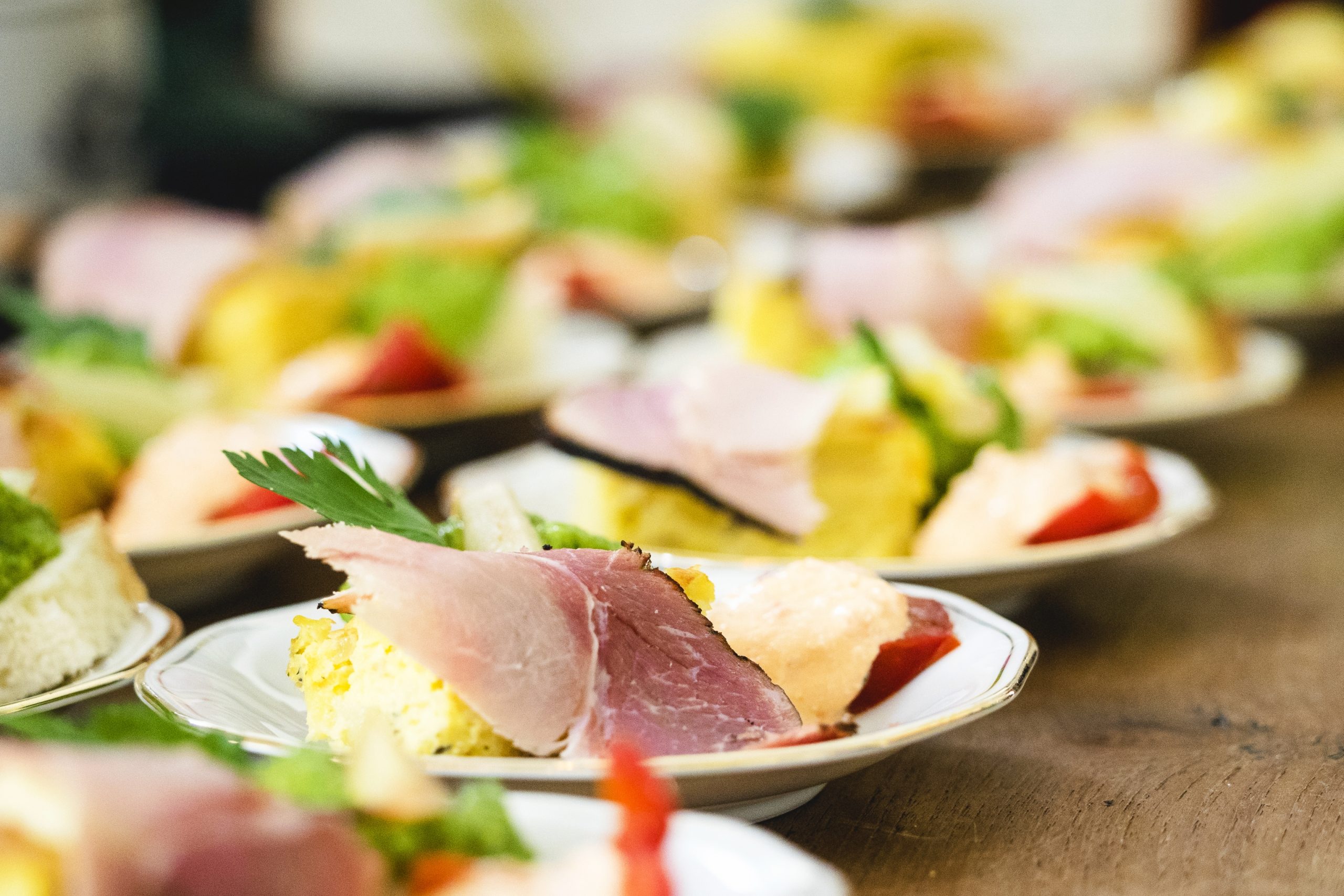 Nahaufnahme von Tellern mit verschiedenen Vorspeisen, darunter Schinken, Gemüse und Tomatenscheiben auf einem Holztisch, die die Essenz der Erlebnisgastronomie einfangen.