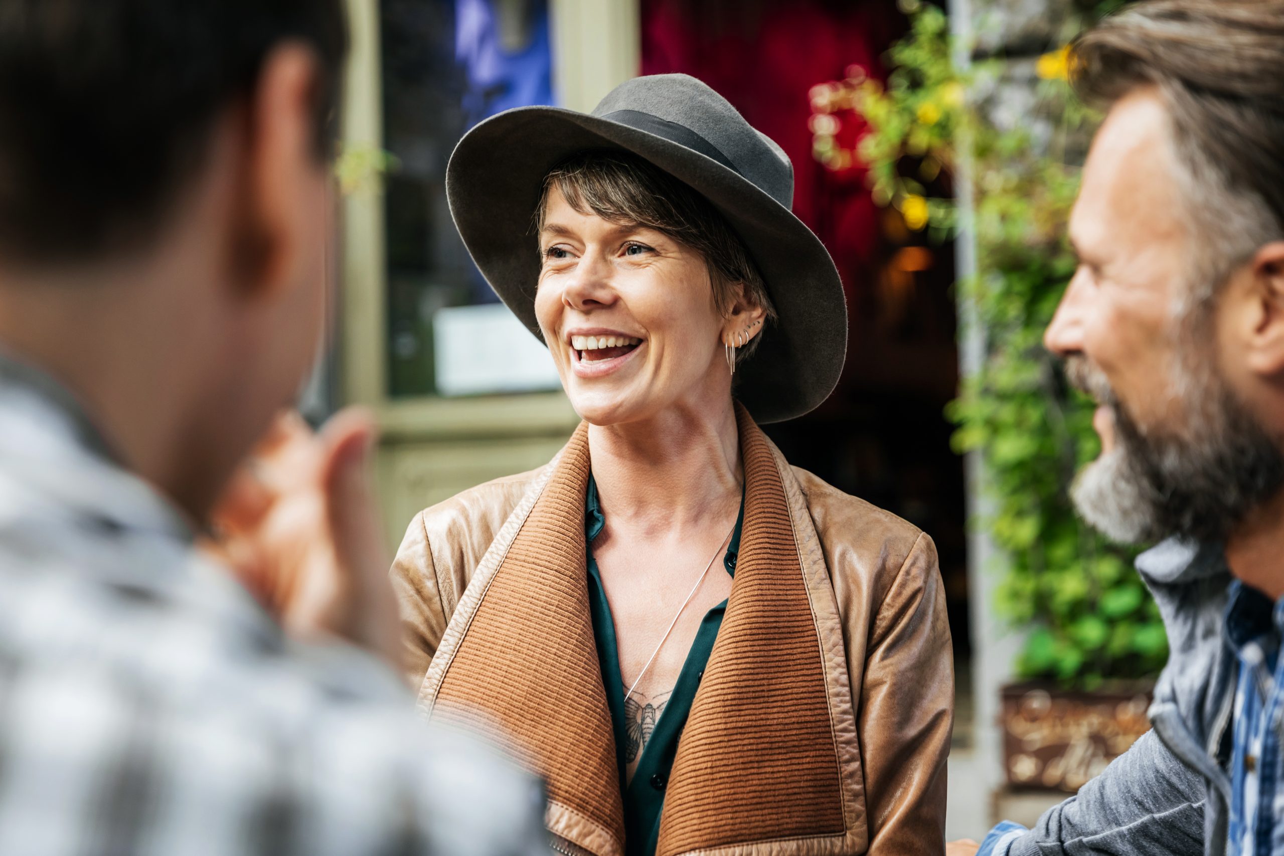 Eine Frau mit Hut lächelt, während sie sich im Freien angeregt mit zwei Menschen unterhält und den Geist der Erlebnisgastronomie verinnerlicht.