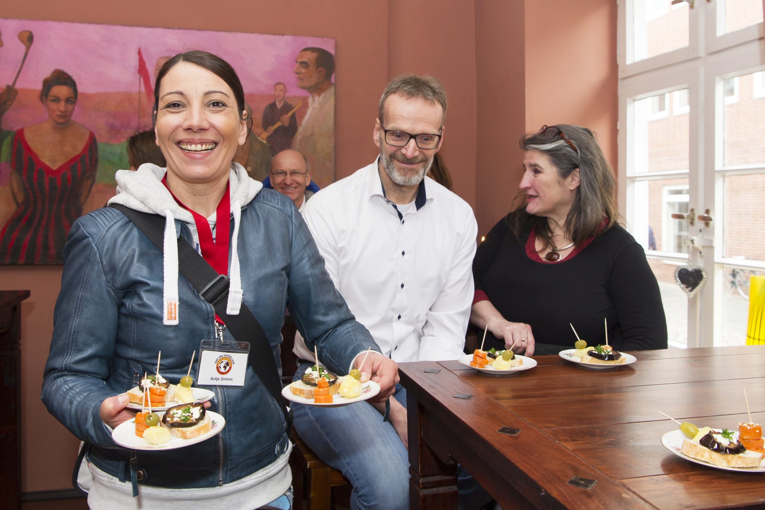 In einem gemütlichen, mit Kunstwerken geschmückten Raum genießen die Menschen ein wunderbares Erlebnisgastronomie-Erlebnis, Essen auf den Tellern und Lächeln auf den Gesichtern, während sie sich herzlich unterhalten.