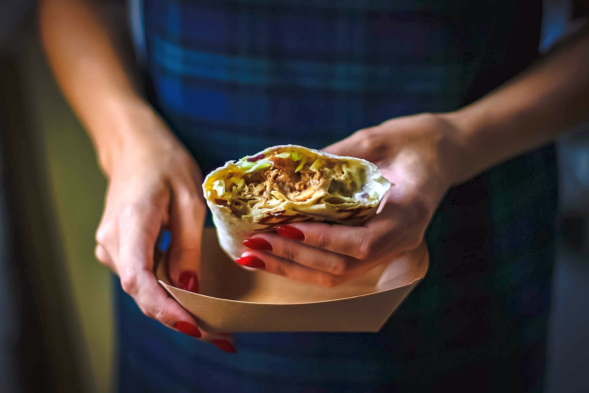 Eine Person genießt einen Leckerbissen aus der Erlebnisgastronomie und hält einen halb aufgegessenen Wrap mit köstlicher Füllung in einer braunen Papierhülle.