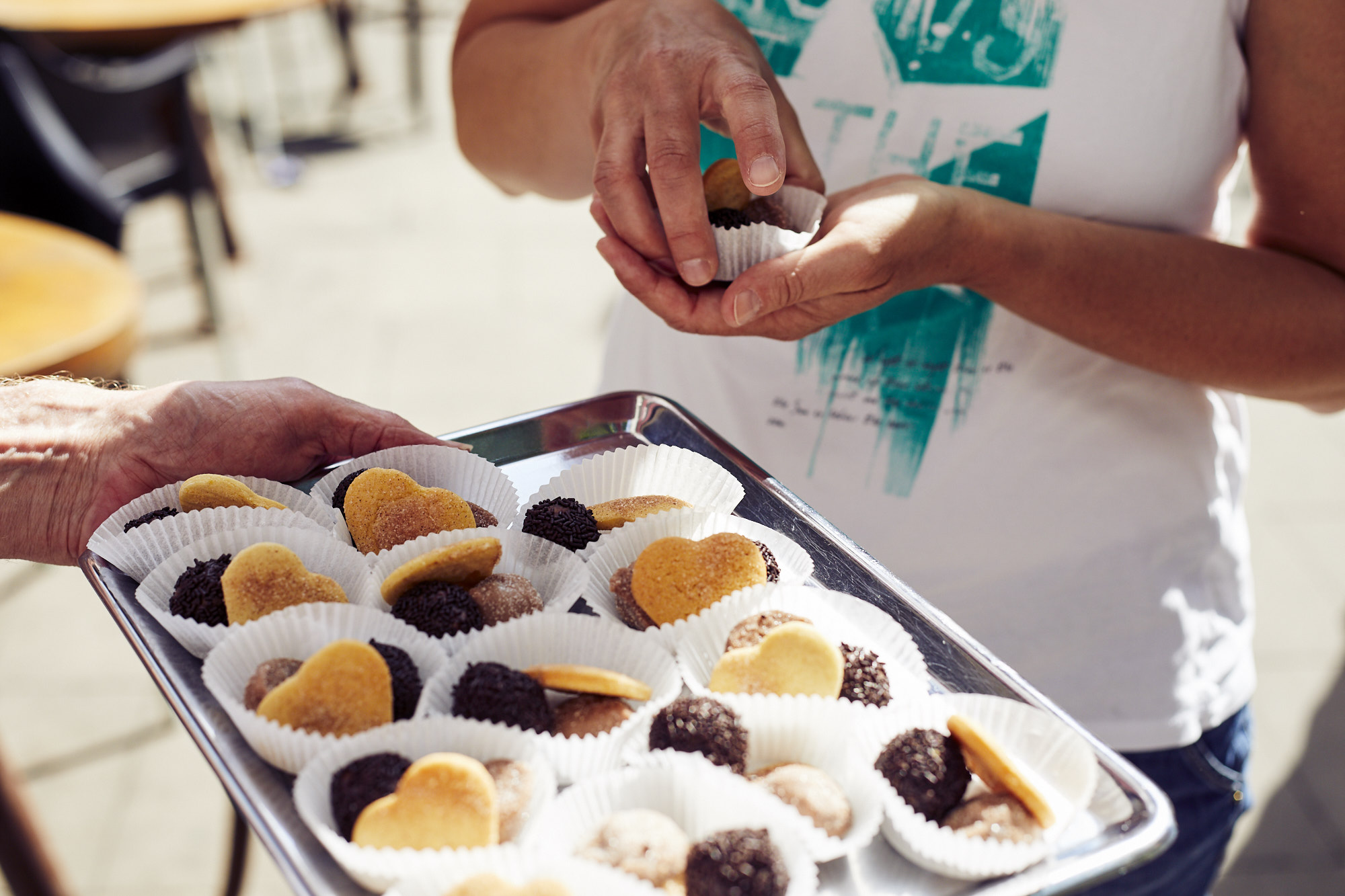 Zwei Personen präsentieren stolz ein Tablett mit verschiedenen runden Desserts in Pappbechern und verkörpern damit den Geist der Erlebnisgastronomie in einer zauberhaften Umgebung im Freien.