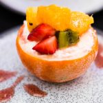 Eine mit Joghurt gefüllte, halbierte Orange, garniert mit Orangenscheiben, Erdbeeren und Kiwi, ergibt eine exquisite Präsentation auf einem dekorativen Teller – ein wahres Erlebnisgastronomie-Erlebnis.