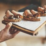 Eine Person hält ein Tablett mit Brot, das mit gerolltem Wurstaufschnitt und Gemüse belegt ist, und bietet ein herrliches Erlebnisgastronomie an.