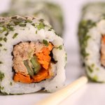 Erleben Sie die Kunst der Erlebnisgastronomie mit dieser Nahaufnahme von Sushi-Rollen mit Reis, Seetang, Thunfisch, Karotte und Avocado, alle garniert mit frisch gehackten Kräutern.