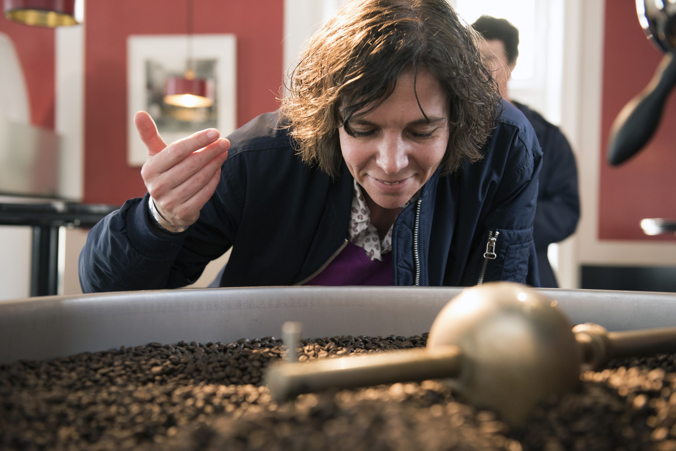 In einem warm beleuchteten Raum, der der Erlebnisgastronomie gewidmet ist, beugt sich eine Person über einen Behälter voller Kaffeebohnen und scheint deren reiches Aroma zu genießen.