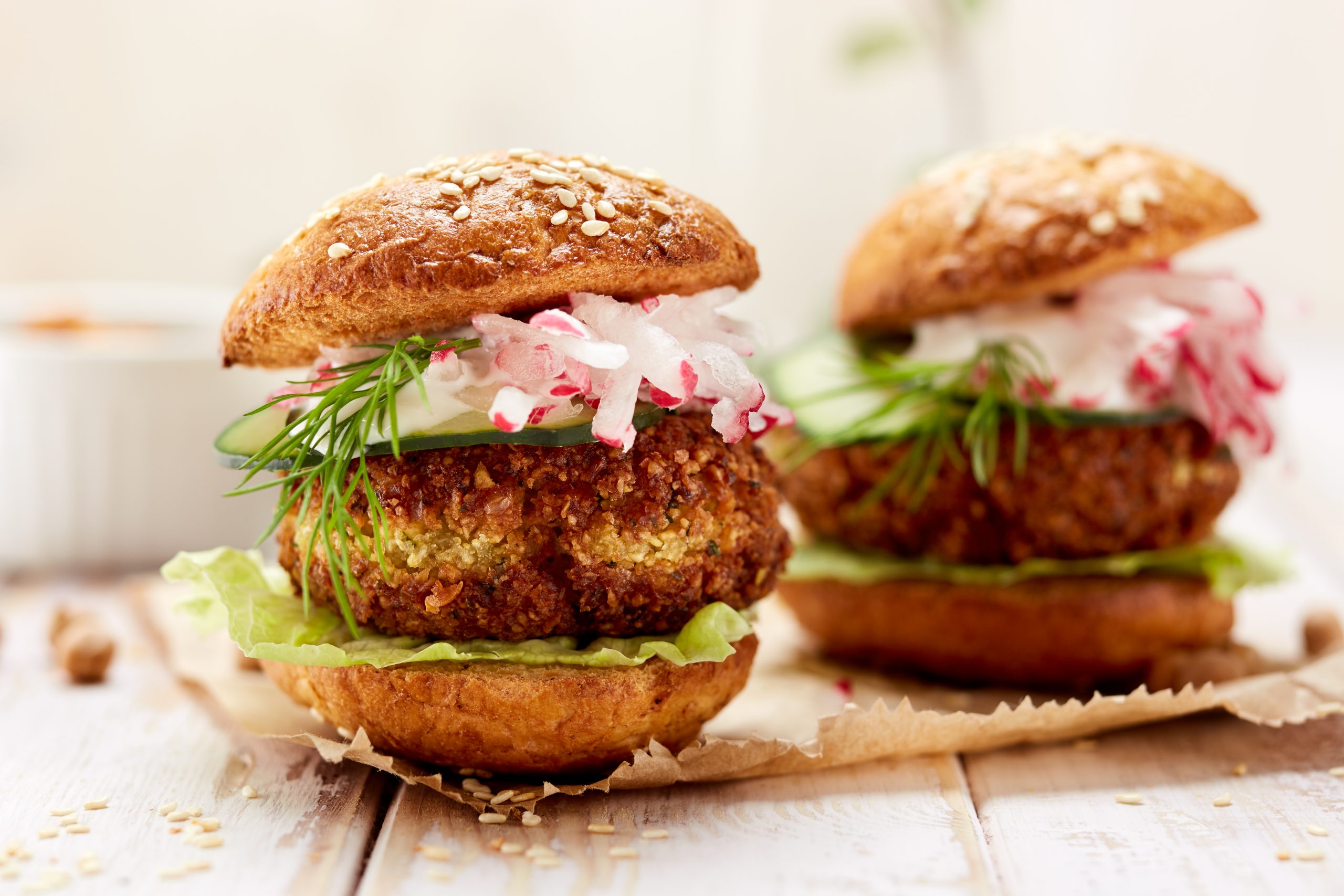 Zwei Gourmet-Veggie-Burger, die den Geist der Erlebnisgastronomie verkörpern, bestehen aus knackigem Salat, Radieschen und Dill, eingebettet in Sesambrötchen auf einem rustikalen Holztisch.