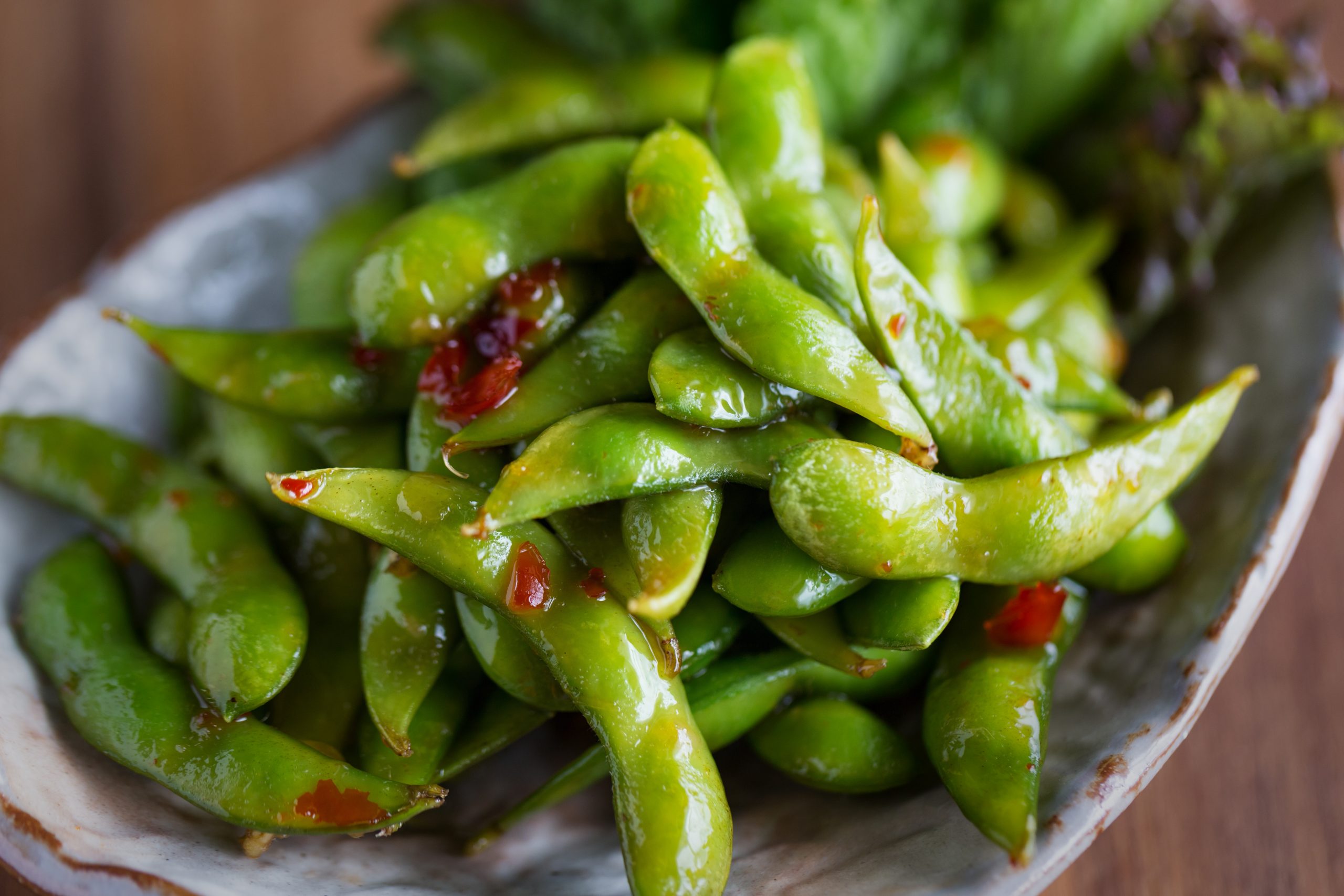 Ein Teller mit scharf gewürzten Edamame-Schoten, garniert mit roten Chiliflocken, bietet einen Vorgeschmack auf die Erlebnisgastronomie, bei der jeder Bissen zu einem unvergesslichen kulinarischen Abenteuer wird.