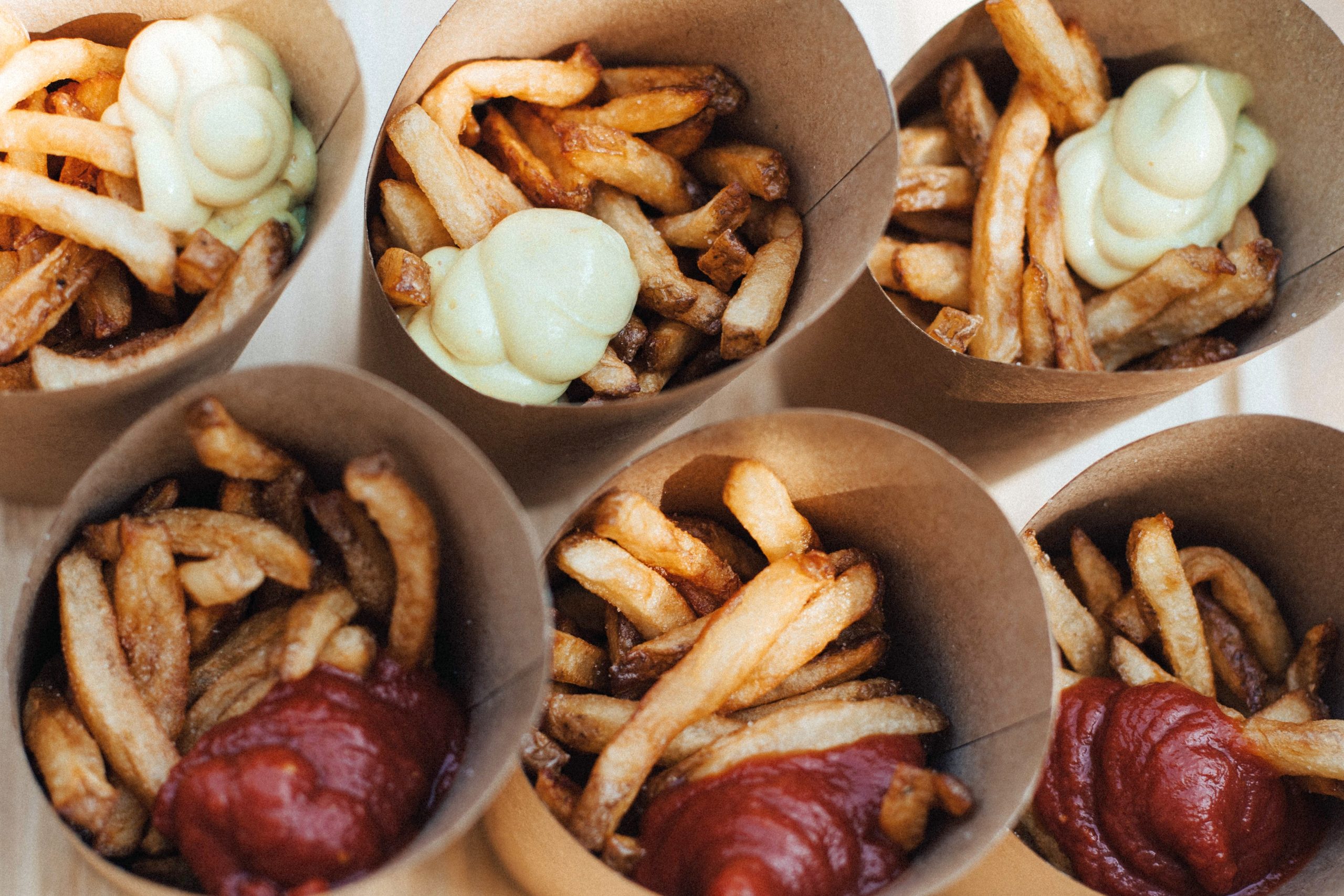 Sechs Papiertüten gefüllt mit Pommes frites, garniert mit Ketchup und Mayonnaise, bringen einen Hauch Erlebnisgastronomie in Ihre Mahlzeit.