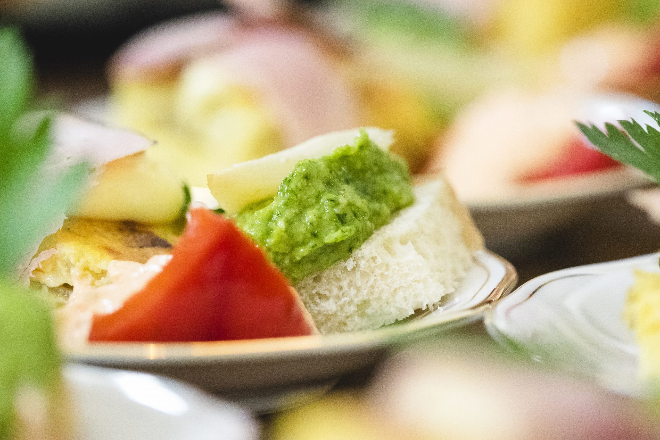 Eine Nahaufnahme eines Tellers mit Sandwiches mit grünem Aufstrich, Käse und Tomate fängt die Essenz der Erlebnisgastronomie vor einem sanft verschwommenen Hintergrund ein und lädt Sie ein, jede handwerklich hergestellte Schicht zu genießen.