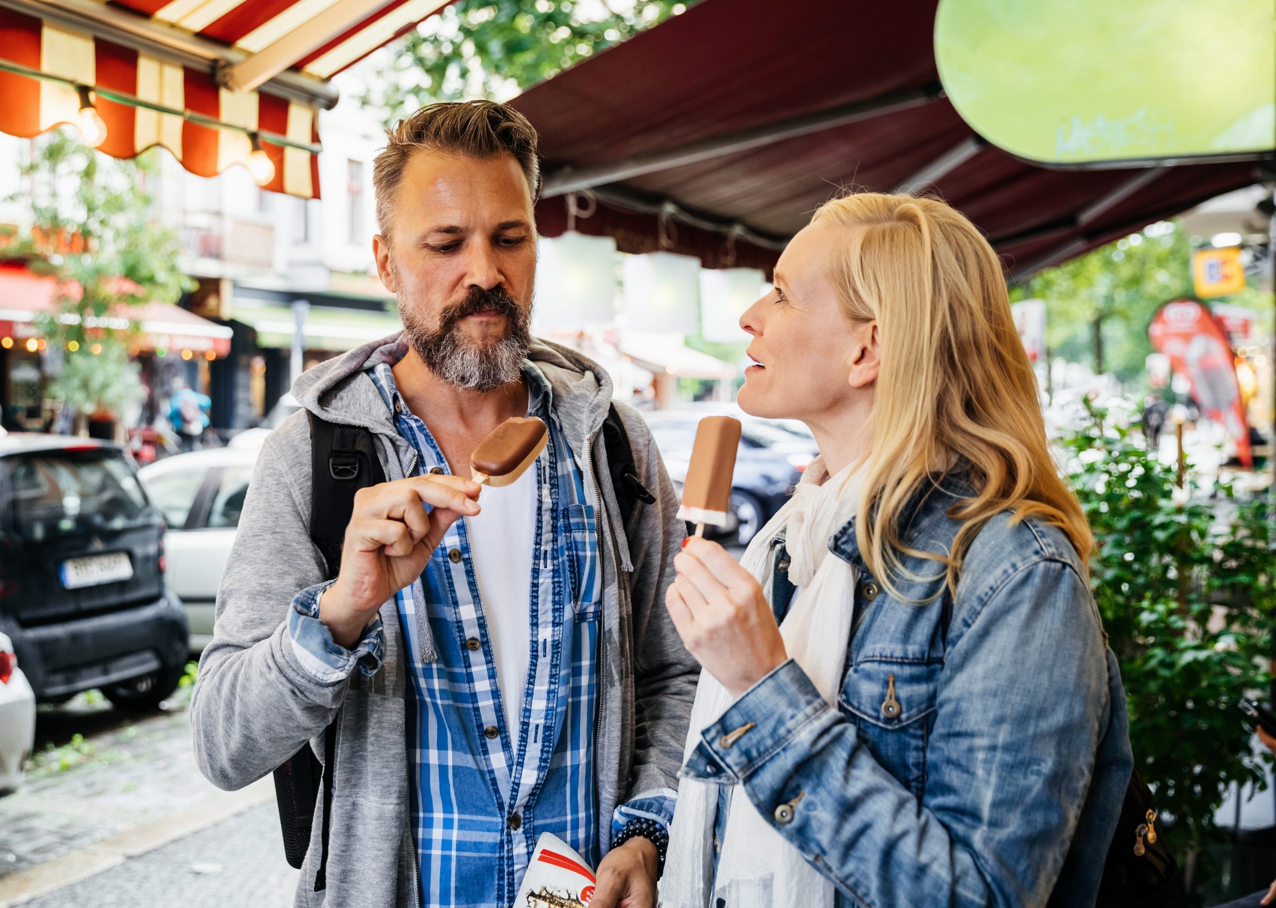 Ein Mann und eine Frau genießen ihr Eis, schlendern unter Markisen durch eine Stadtstraße und verwandeln einen gewöhnlichen Tag in ein erlebnisgastronomisches Vergnügen.