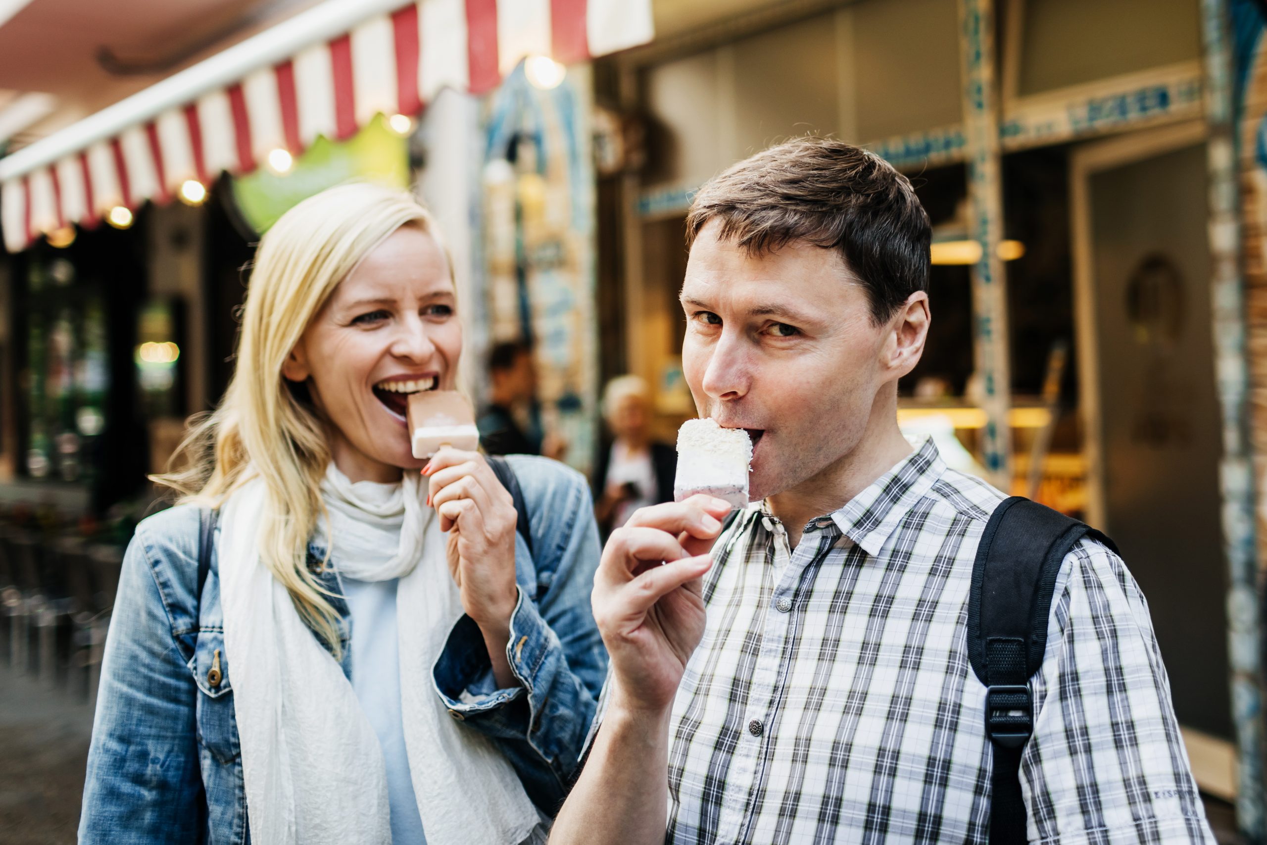 Ein Mann und eine Frau genießen ihr Eis und einen herrlichen Moment der Erlebnisgastronomie, während sie durch die belebte Stadtstraße schlendern.