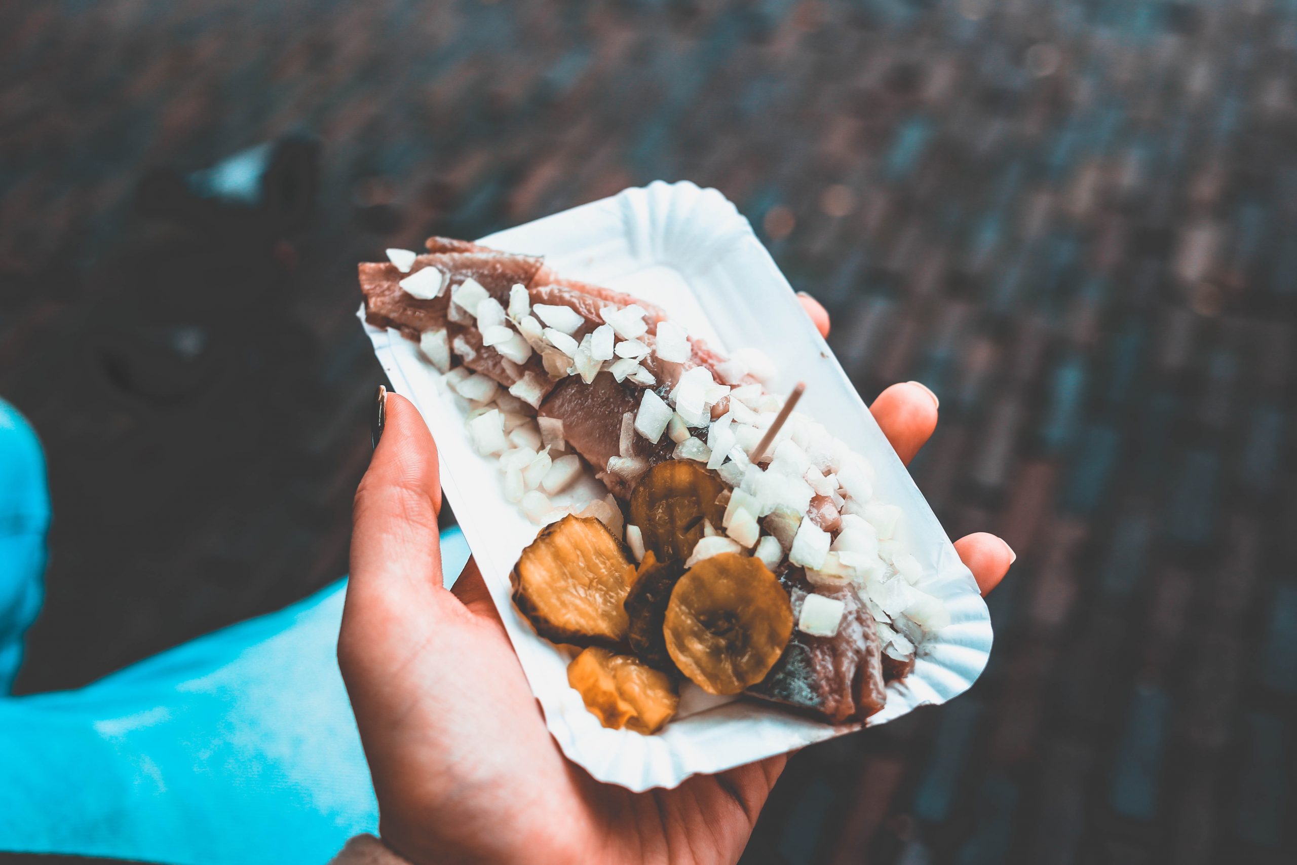 Eine Hand präsentiert anmutig ein Tablett mit Fisch, garniert mit gehackten Zwiebeln und Gurken – eine wunderbare Geschenkidee für kulinarische Enthusiasten.