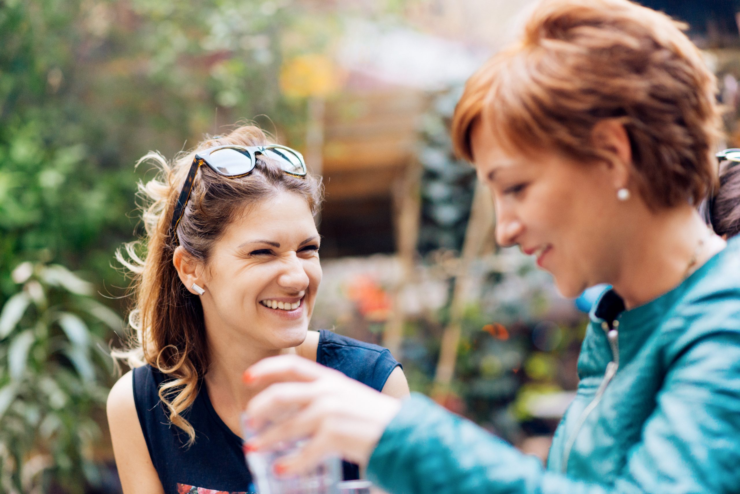 Zwei Frauen unterhalten sich und lächeln im Freien, eine hält eine Wasserflasche in der Hand – ein herrlicher Moment, der sich inmitten des üppigen Grüns im Hintergrund wie die perfekte Geschenkidee anfühlt.