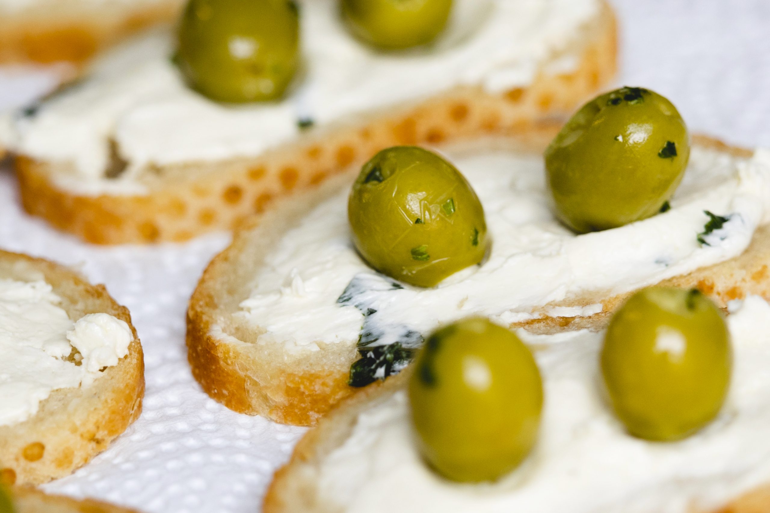 Mit Frischkäse und grünen Oliven belegte Crostini, elegant auf einem Papiertuch angerichtet, sind eine wunderbare Geschenkidee.