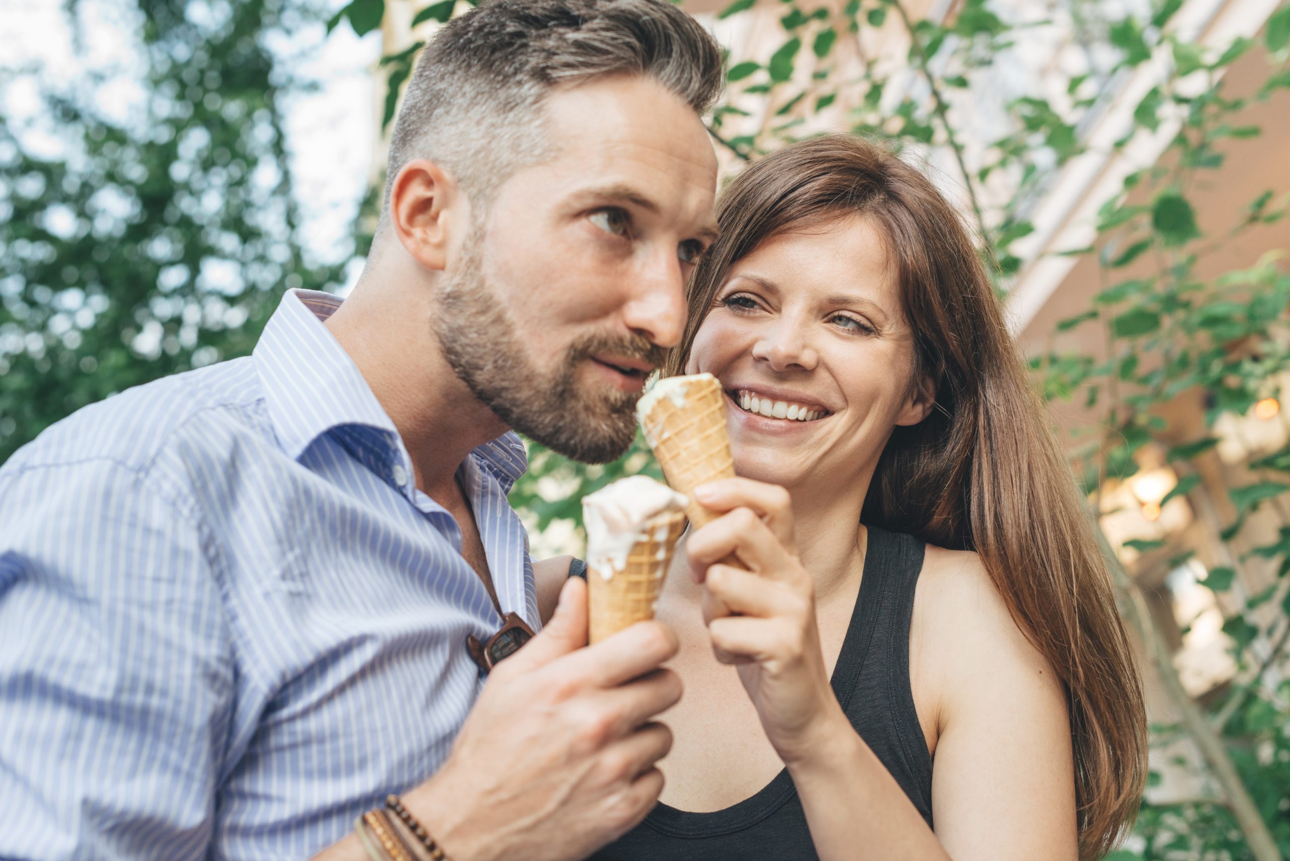 Ein Paar genießt lächelnd und umgeben von üppigem Grün im Freien ein Eis – die perfekte Geschenkidee für einen wunderbaren Tag.