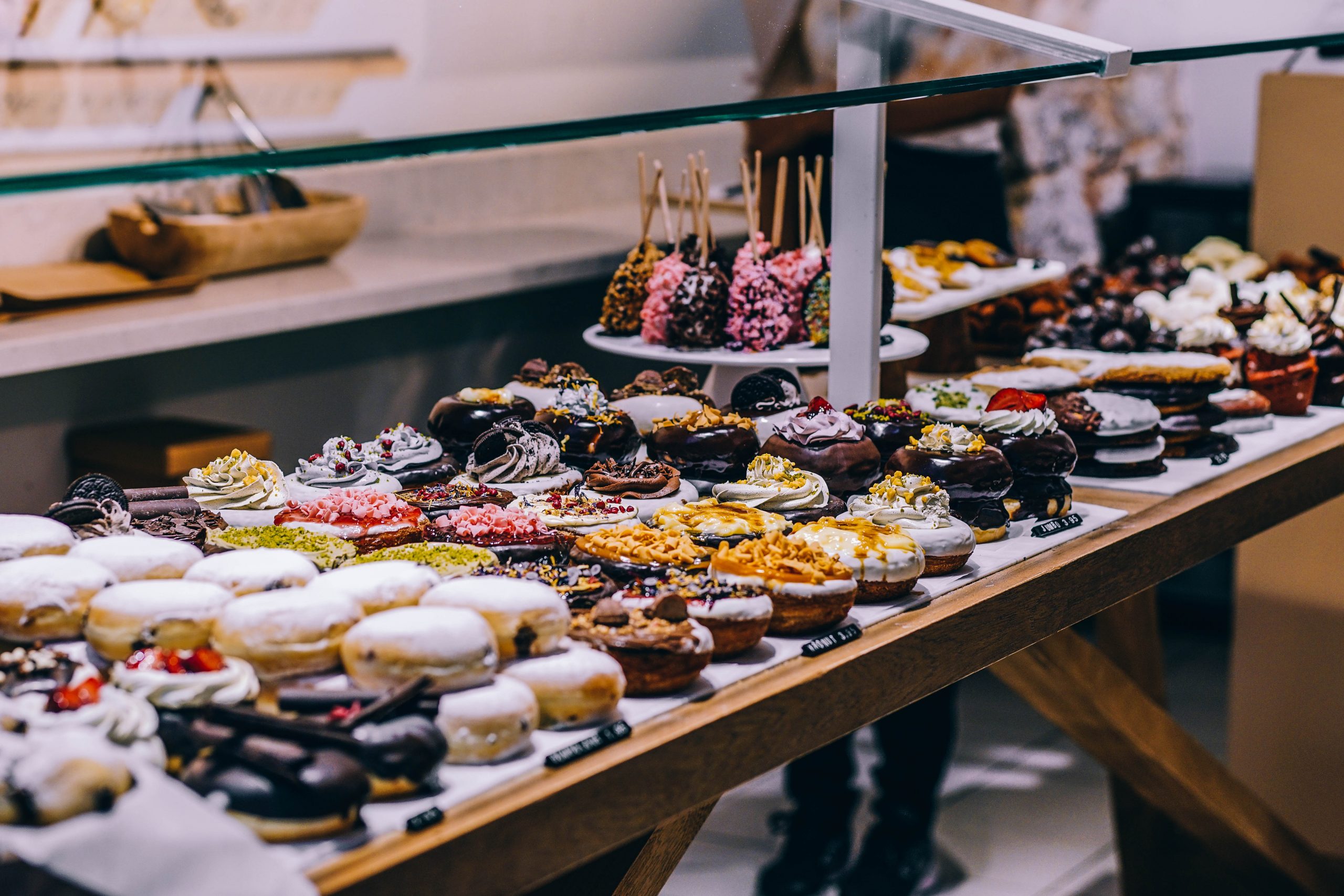 Eine entzückende Auslage verschiedener Donuts und Gebäcke ziert den Holztisch in der Bäckerei, perfekt für alle, die auf der Suche nach einer einzigartigen Geschenkidee sind.