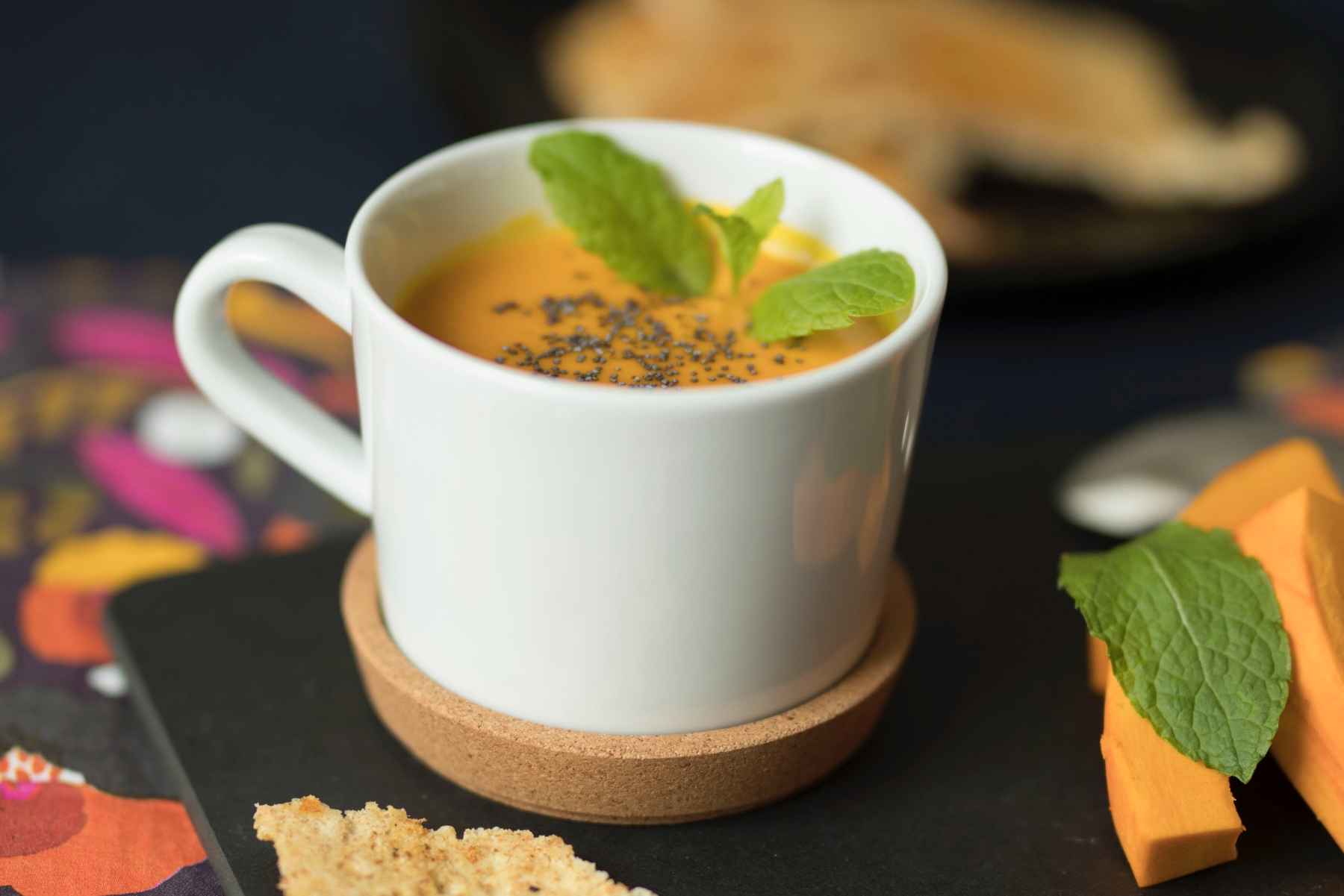 Eine Tasse cremige Orangensuppe, garniert mit Minze und Samen, dazu Brot und Scheibenkäse – eine wunderbare Geschenkidee für jeden Feinschmecker.